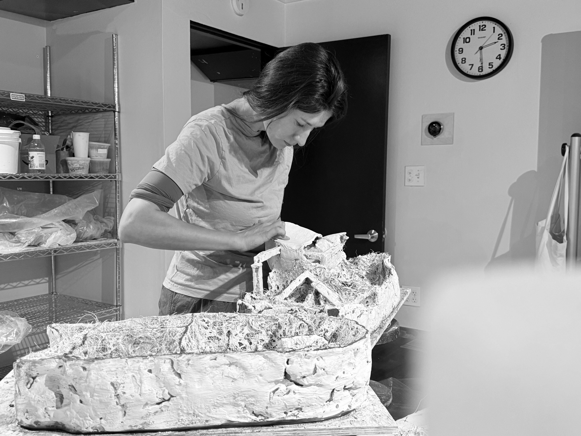 Working on a long hollow cast form packed with pale fibre, on a table in a borrowed studio