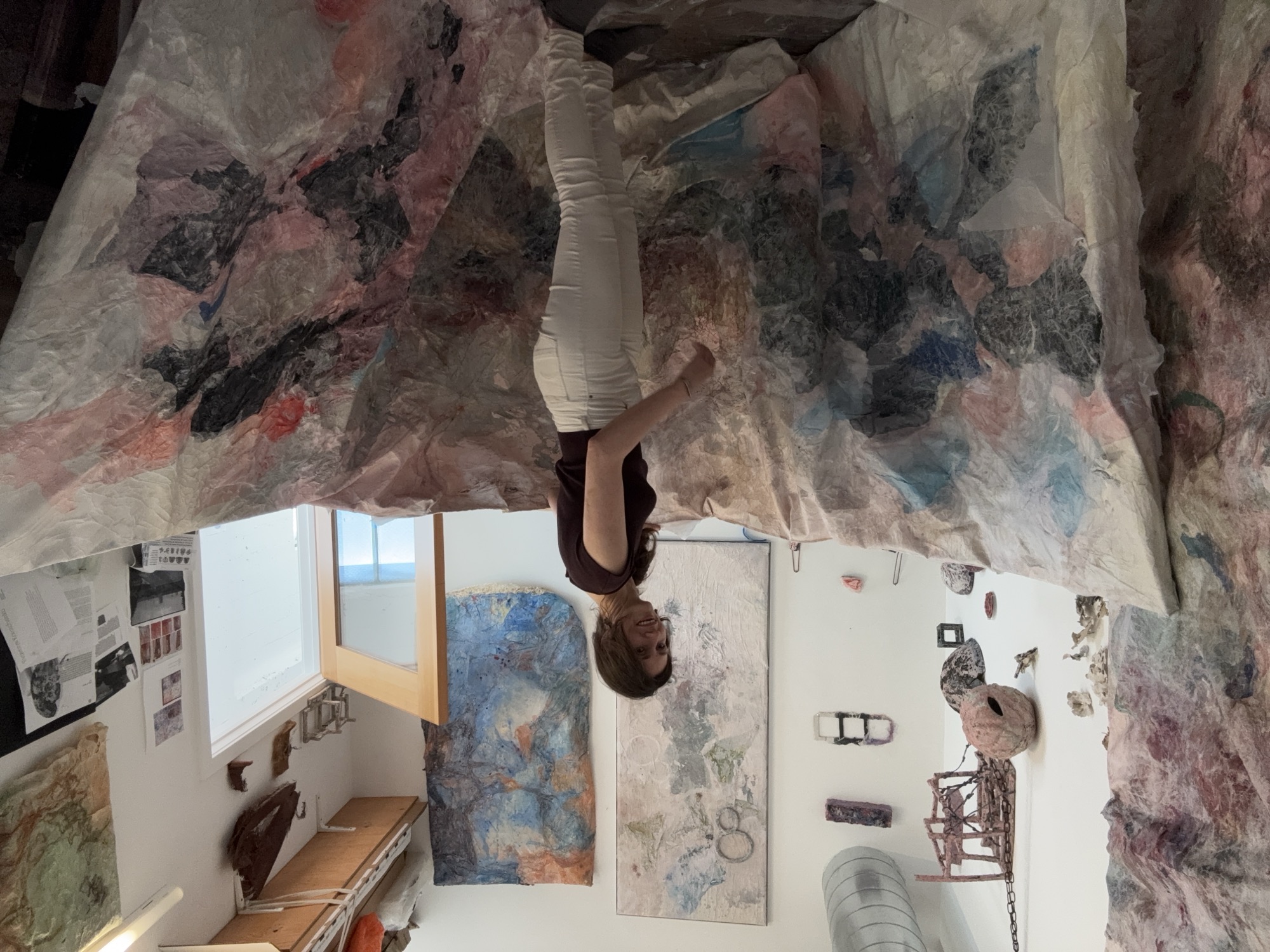 The studio in 2026: large paper works hanging, ceramic pieces mounted on the wall behind