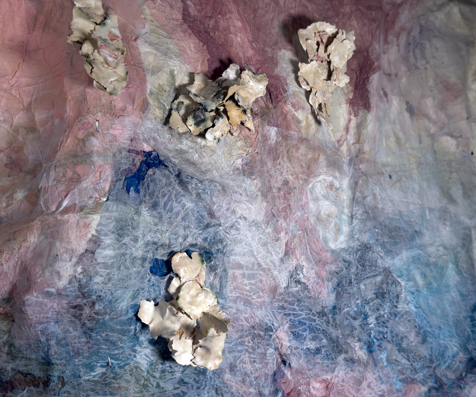 Detail: pale ceramic flakes fused into clusters on the paper ground, where a pink field gives way to blue