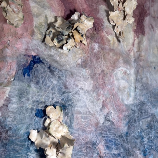Detail: pale ceramic flakes fused into clusters on the paper ground, where a pink field gives way to blue